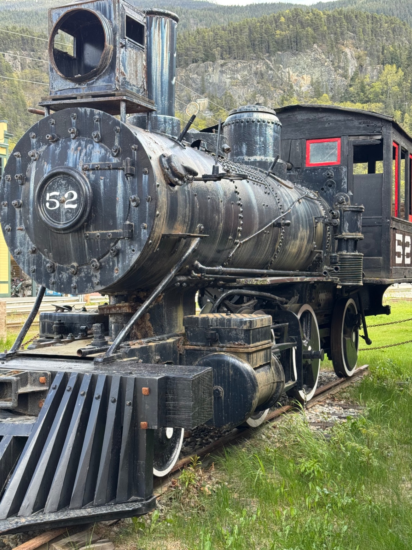 Vintage steam locomotive number 52 with black metal body and red accents displayed in a forested mountain valley