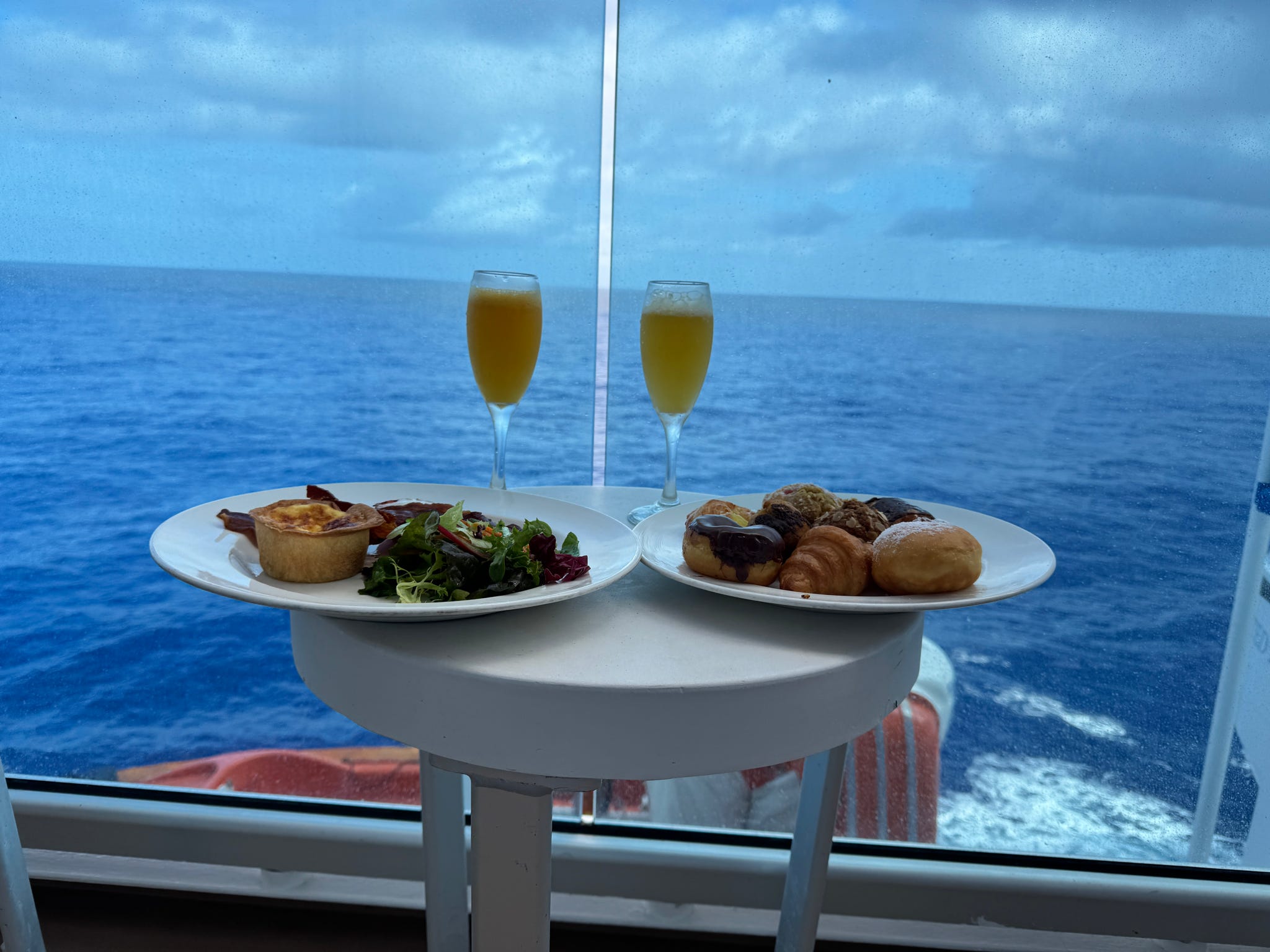 A romantic cruise ship breakfast with mimosas and pastries overlooking the open blue ocean.