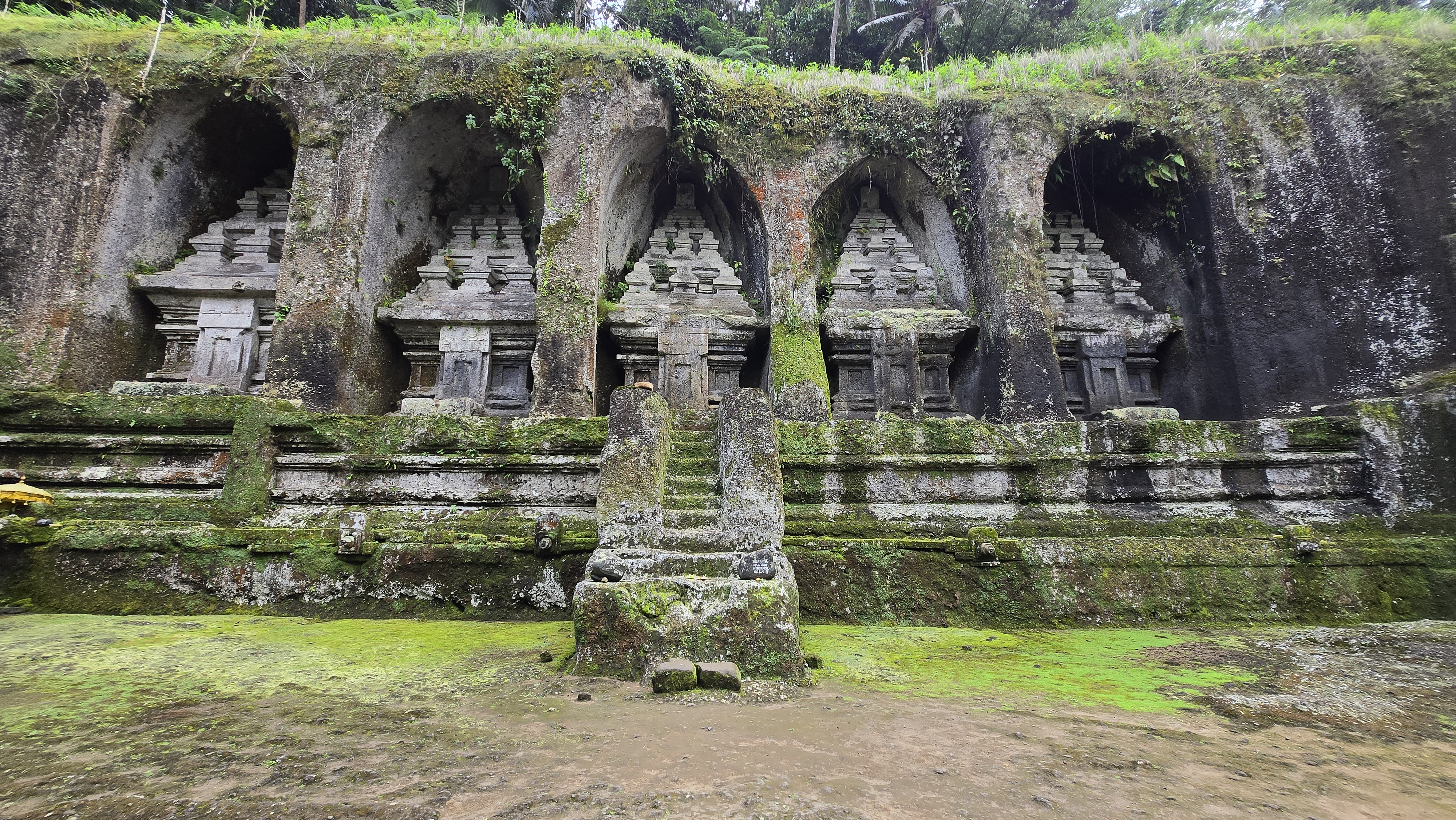 Ancient stone temple ruins with five arched alcoves covered in moss and vegetation, set against a misty green landscape