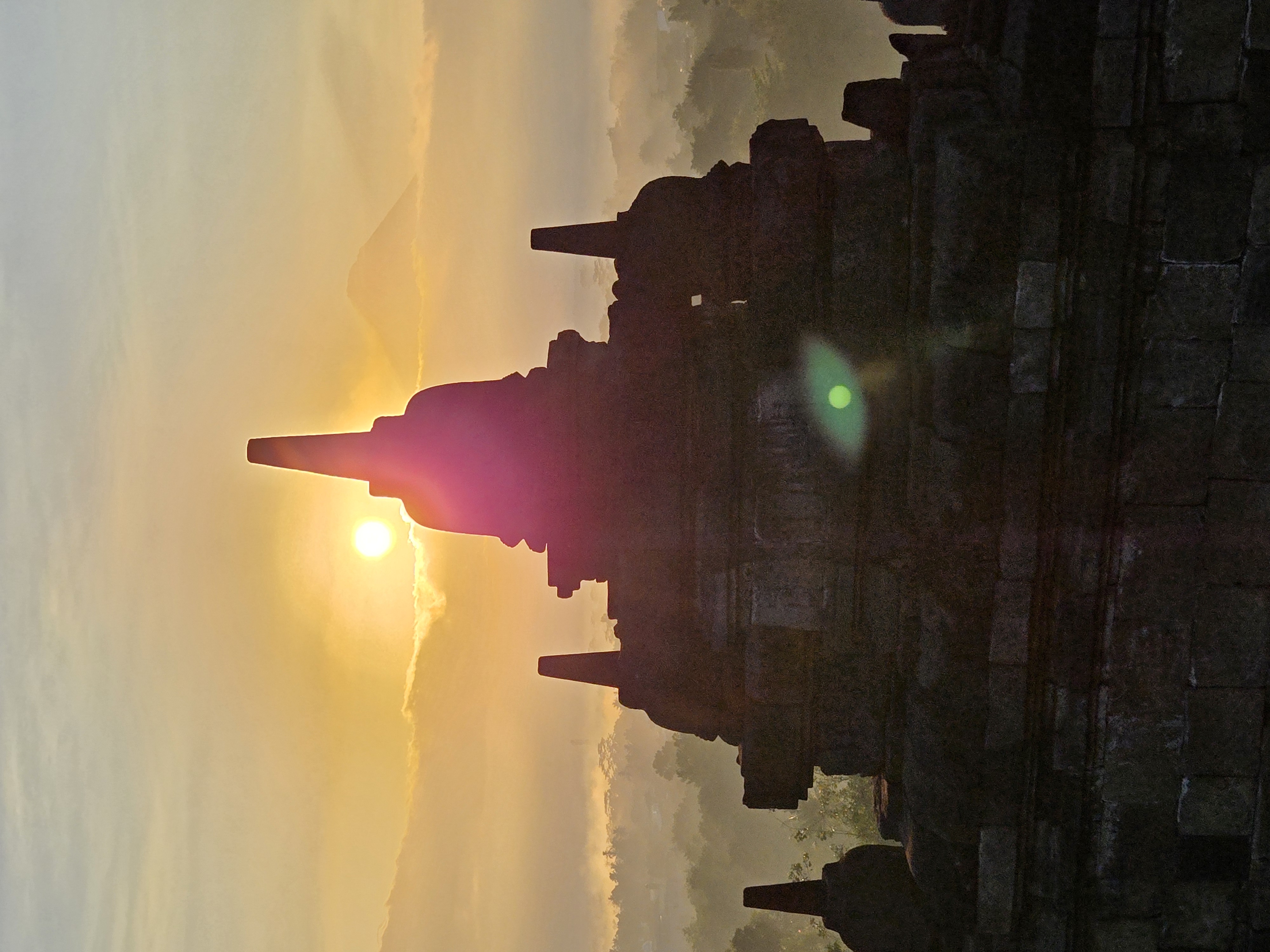 Silhouetted temple structures at dawn with Mount Agung visible through mist in the distance