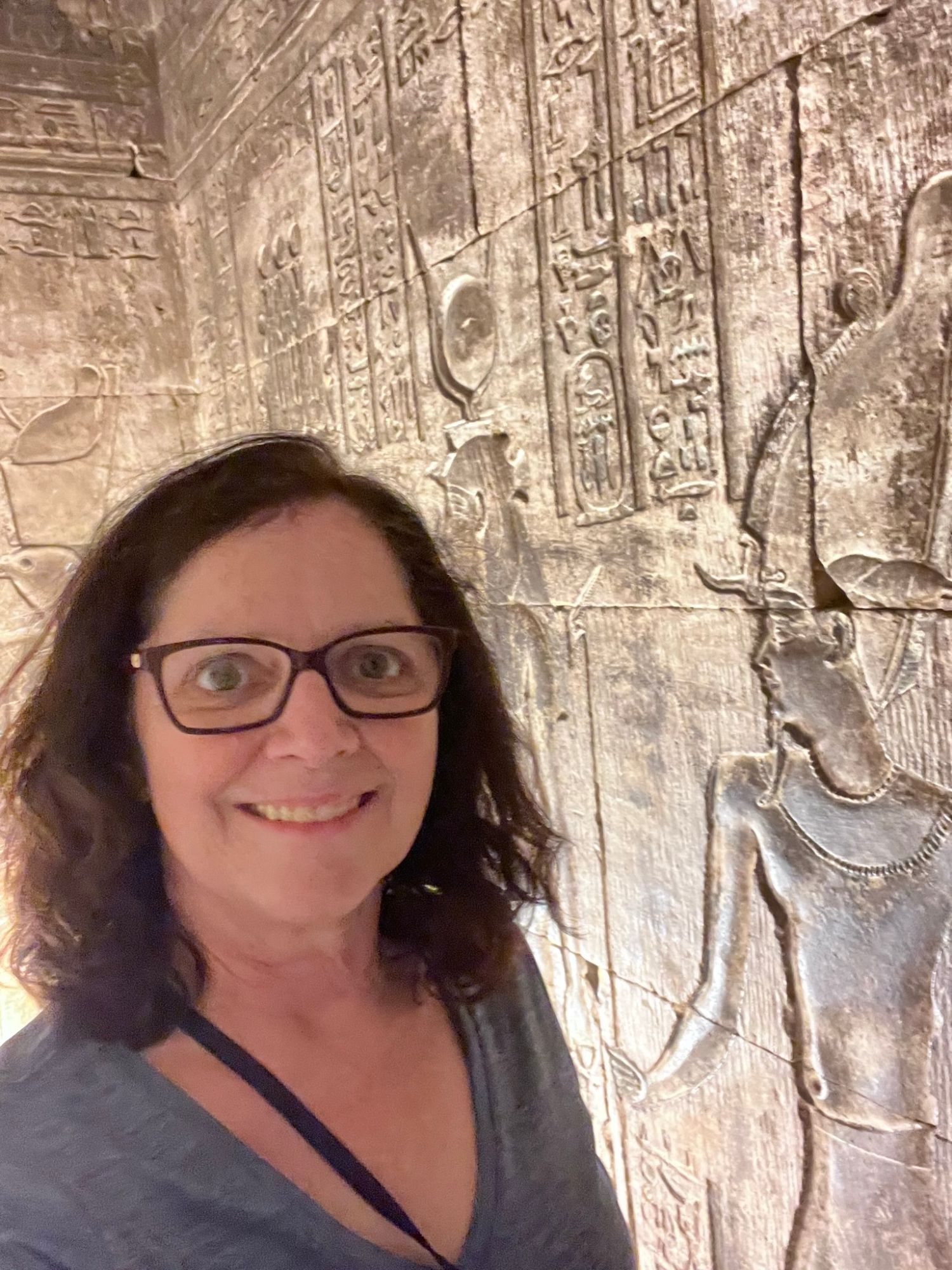 Julie smiling at the camera with Egyptian hieroglyphic carvings visible on the stone wall behind her