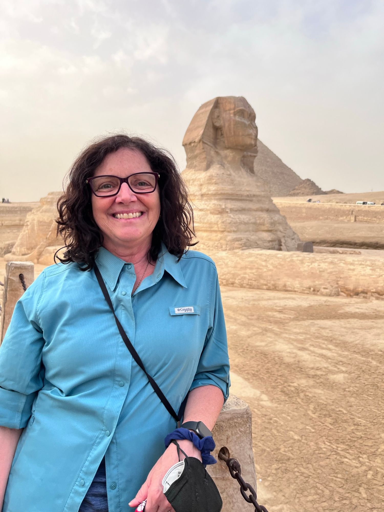 Julie in a blue shirt smiling at the camera with the Great Sphinx visible behind her in the desert