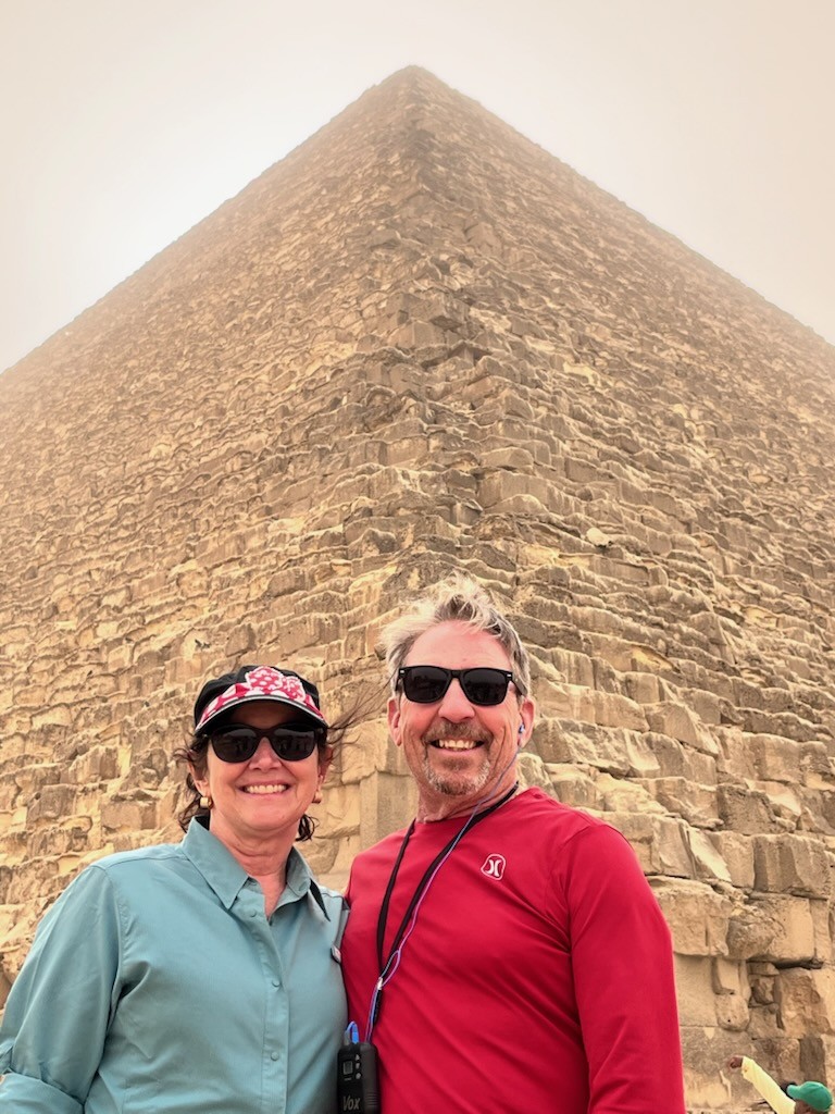 Group of eight people posing together in front of a large pyramid at Giza, Egypt