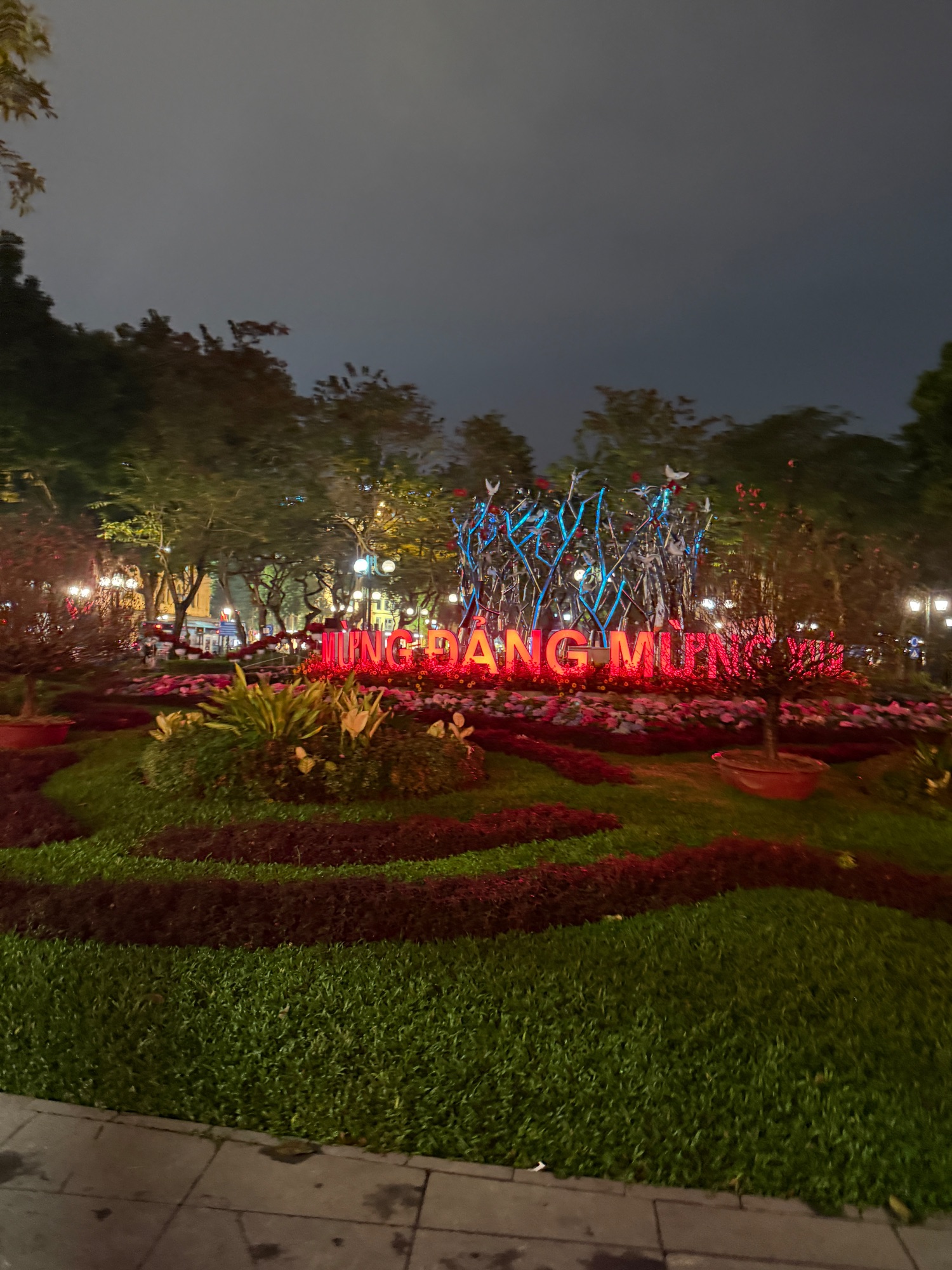 Illuminated red sign reading 'HUNG PHUONG MIEN' in a park at dusk with blue-lit trees and manicured landscaping