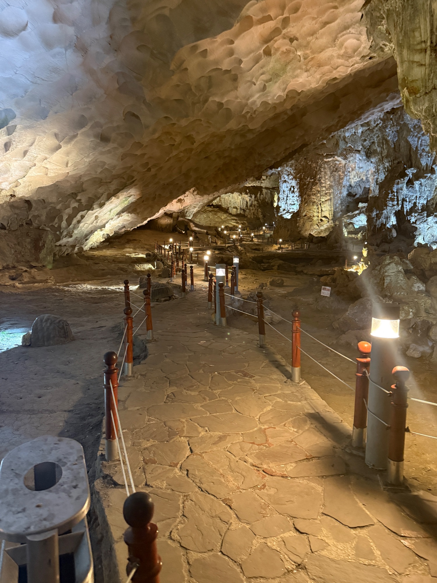 Illuminated cave interior with wooden walkway, metal railings, and dramatic natural rock formations overhead