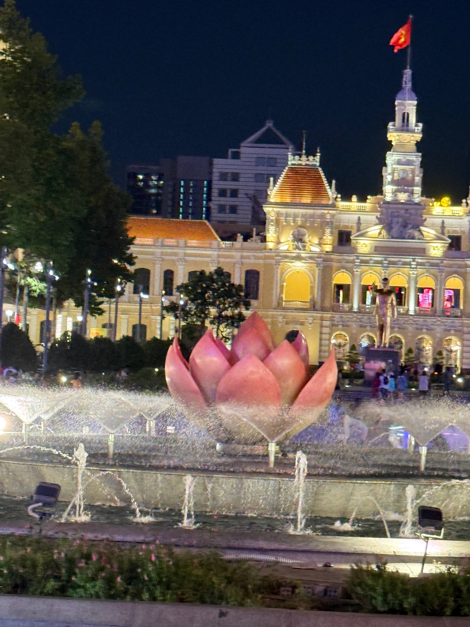 Nighttime view of Ho Chi Minh City's illuminated colonial City Hall with pink lotus sculpture and fountains