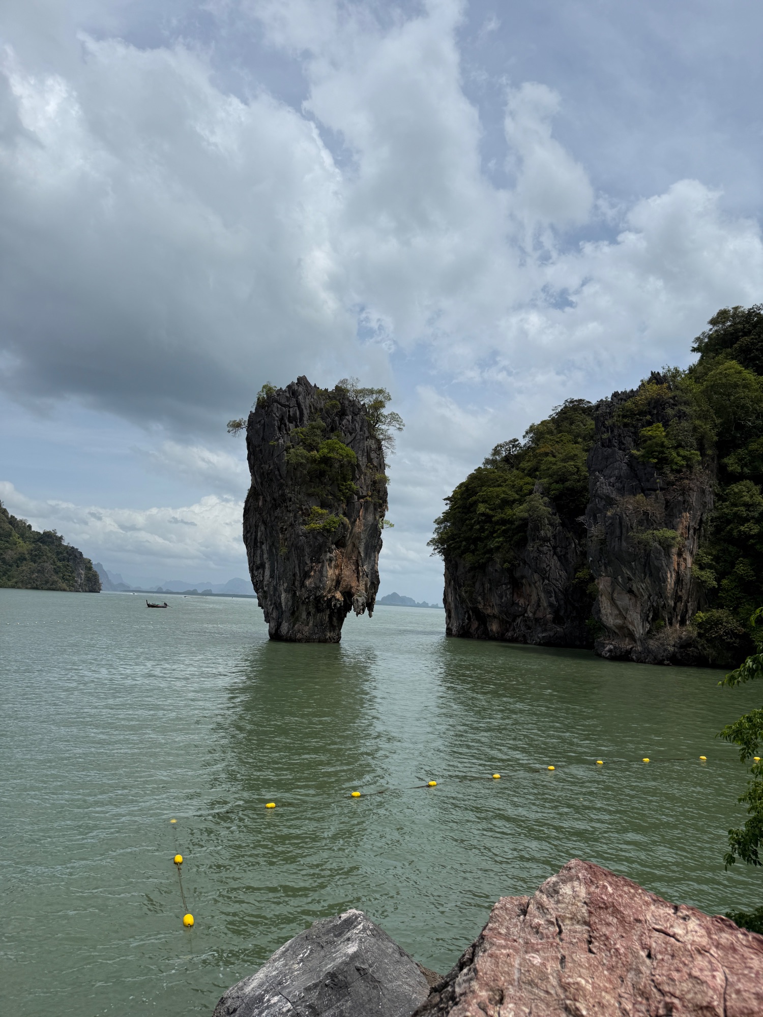 Dramatic limestone rock formations rising from turquoise water with a small boat and yellow buoys in the foreground