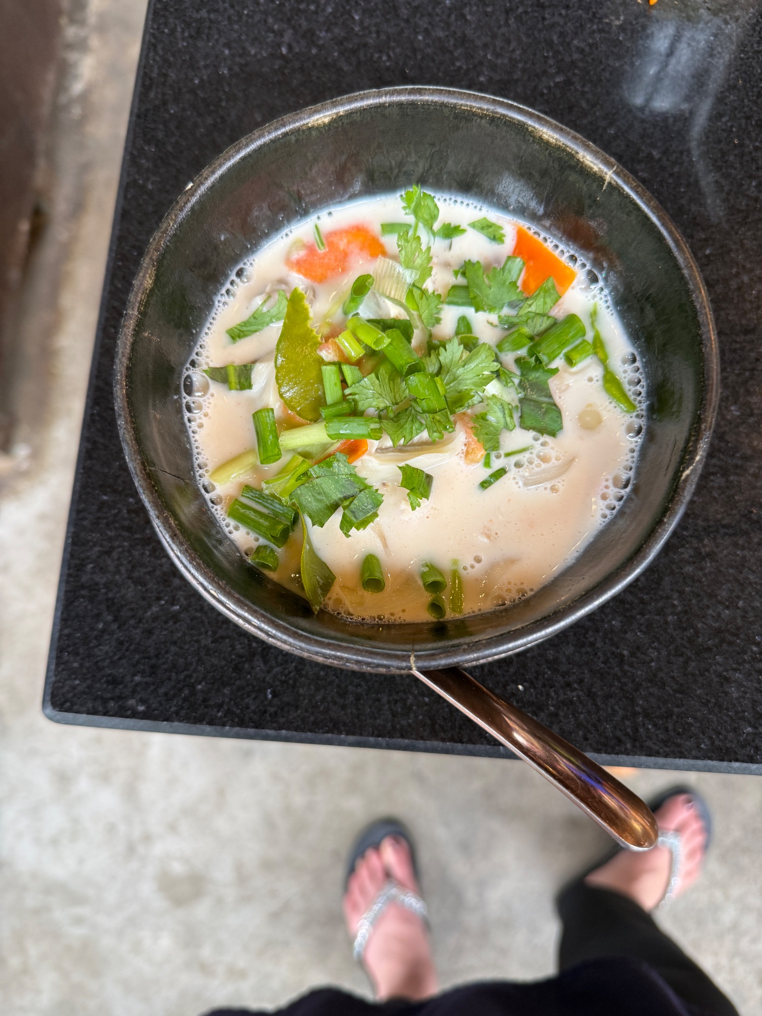 Creamy Thai soup in a dark bowl garnished with green onions and cilantro on a black surface