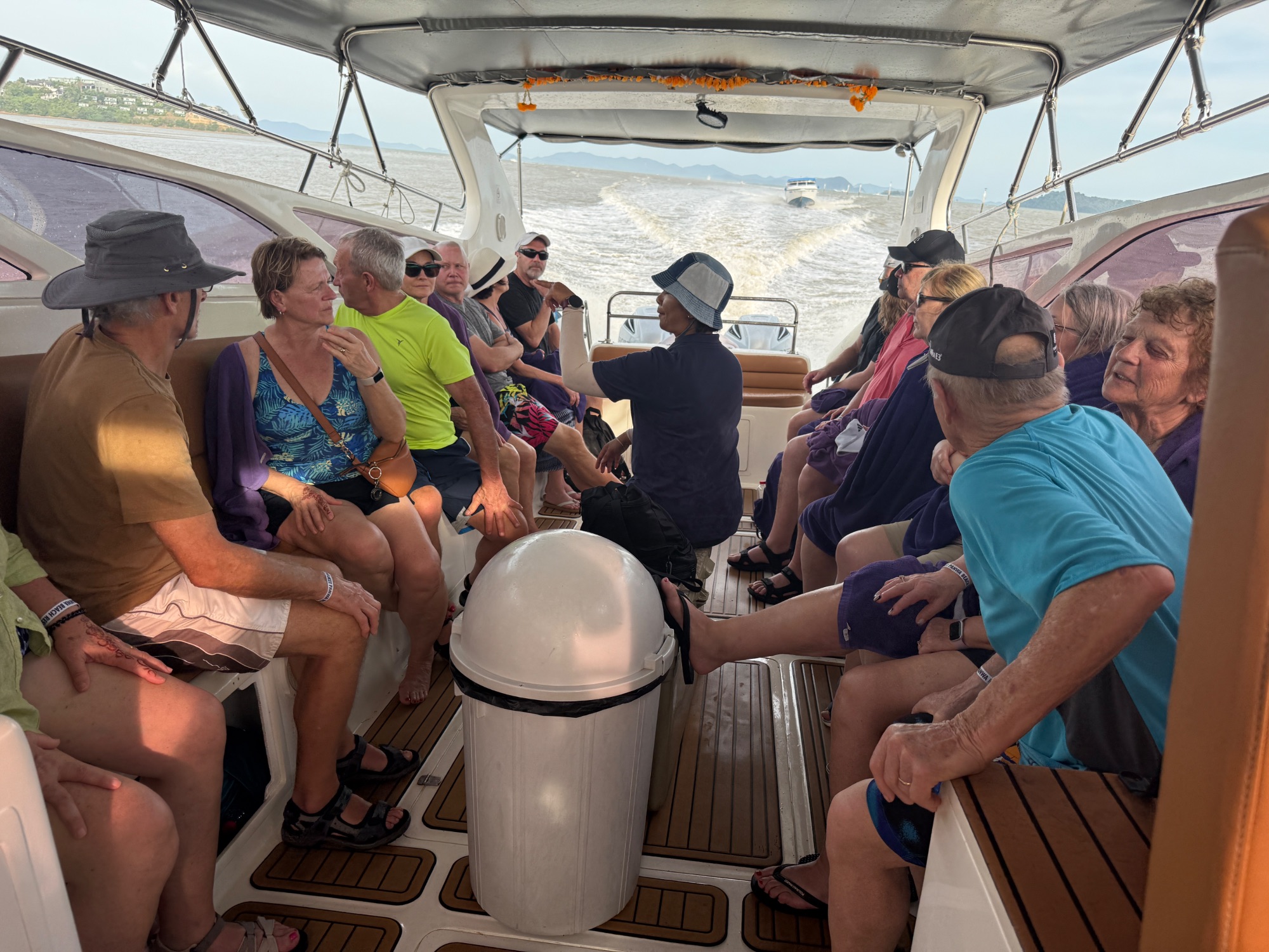 Group of tourists seated inside a covered boat during a daytime excursion on calm water