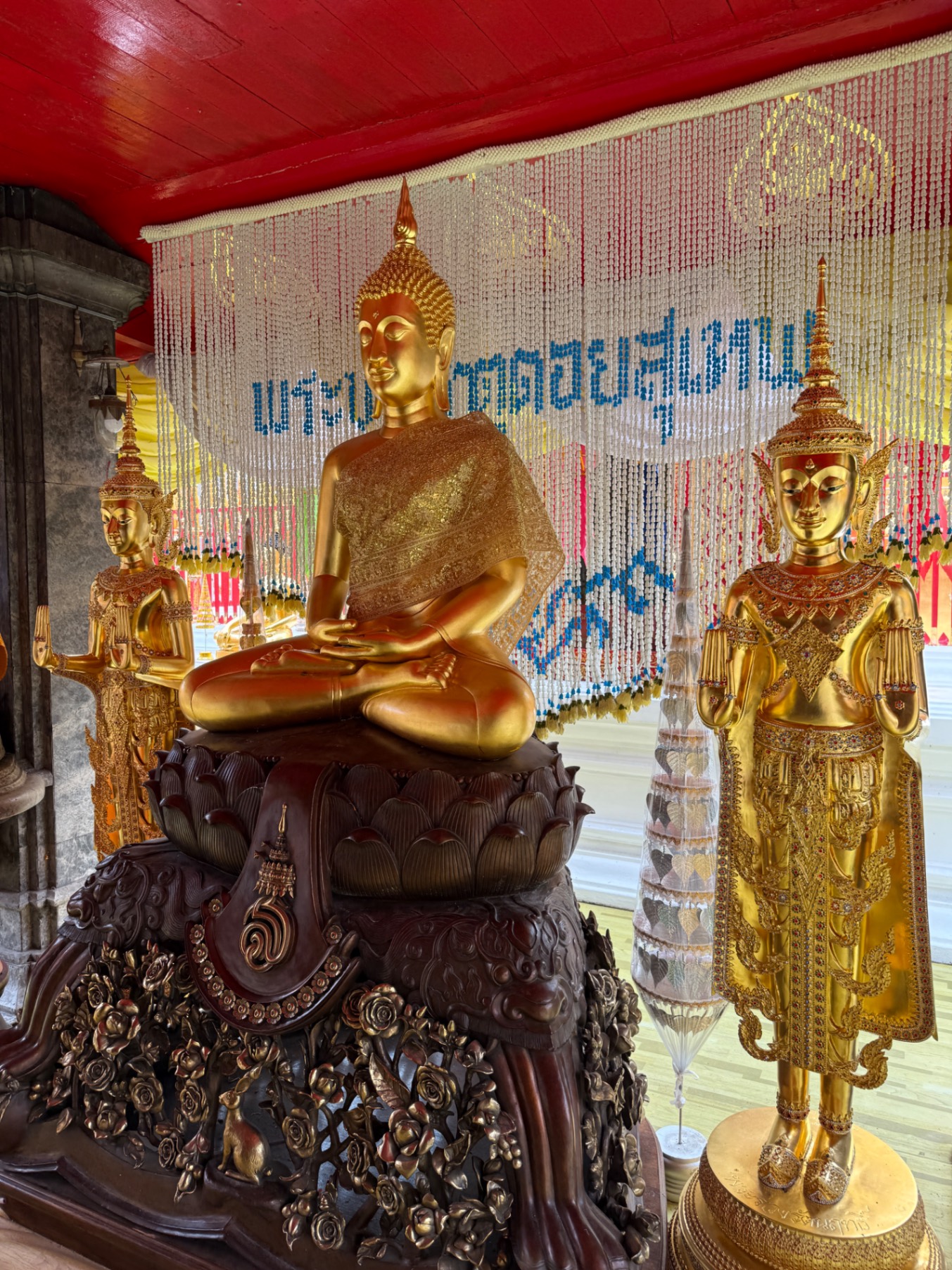 Golden tiered pagoda with intricate details and pointed spire at a Thai temple with visitors gathered nearby