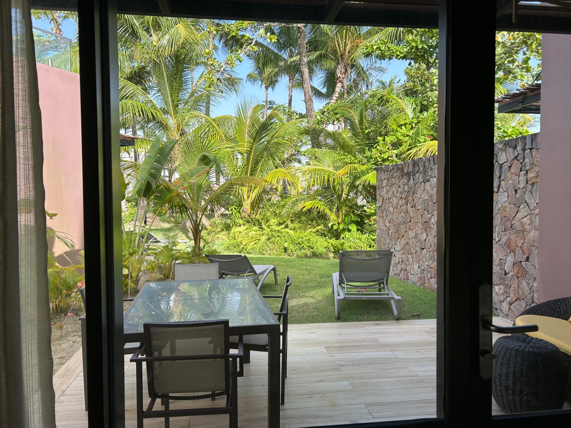 Tropical garden view through large glass doors with palm trees and lounge chairs on lawn