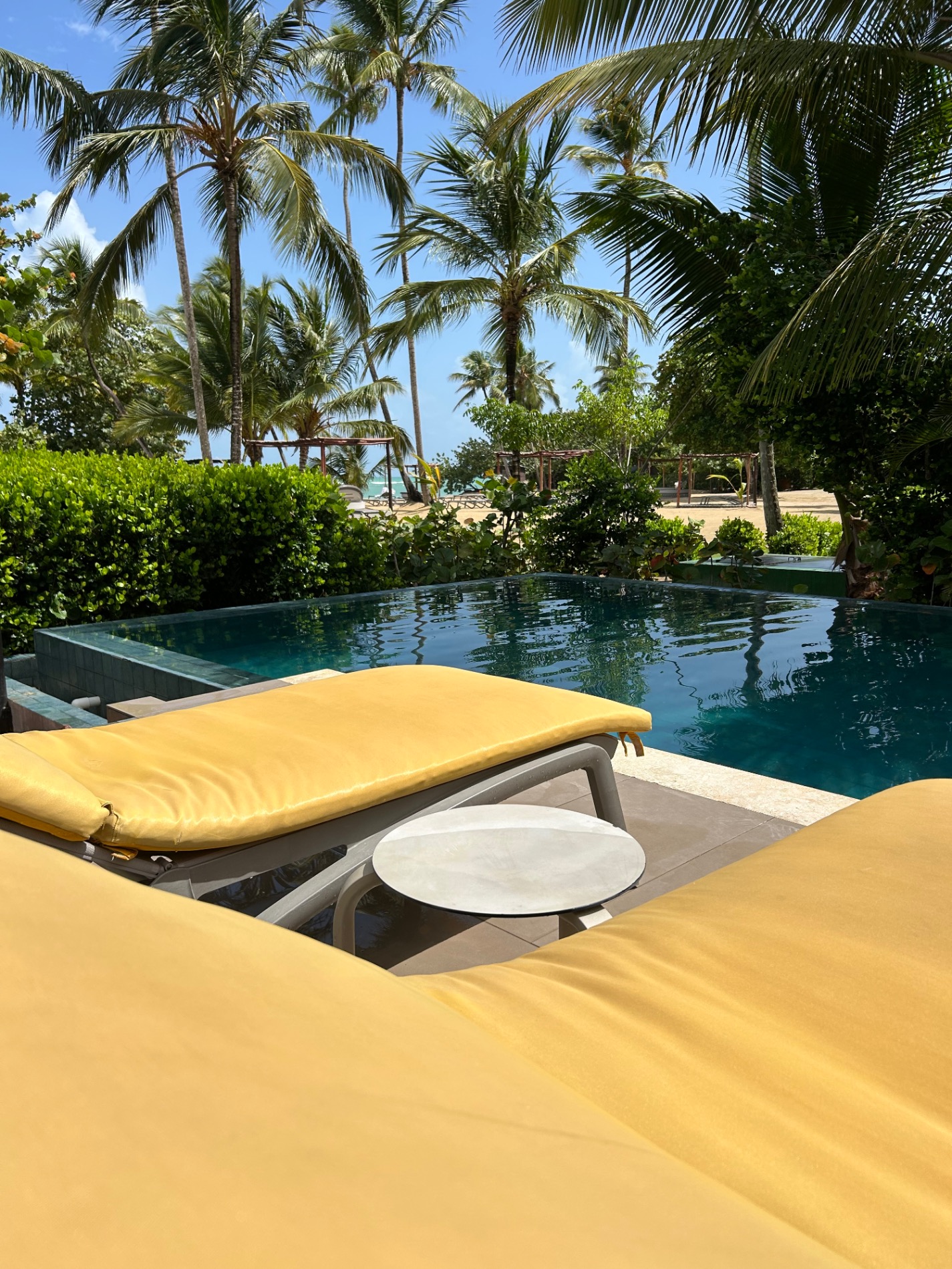 Yellow lounge chair in foreground overlooking turquoise infinity pool and tropical landscape