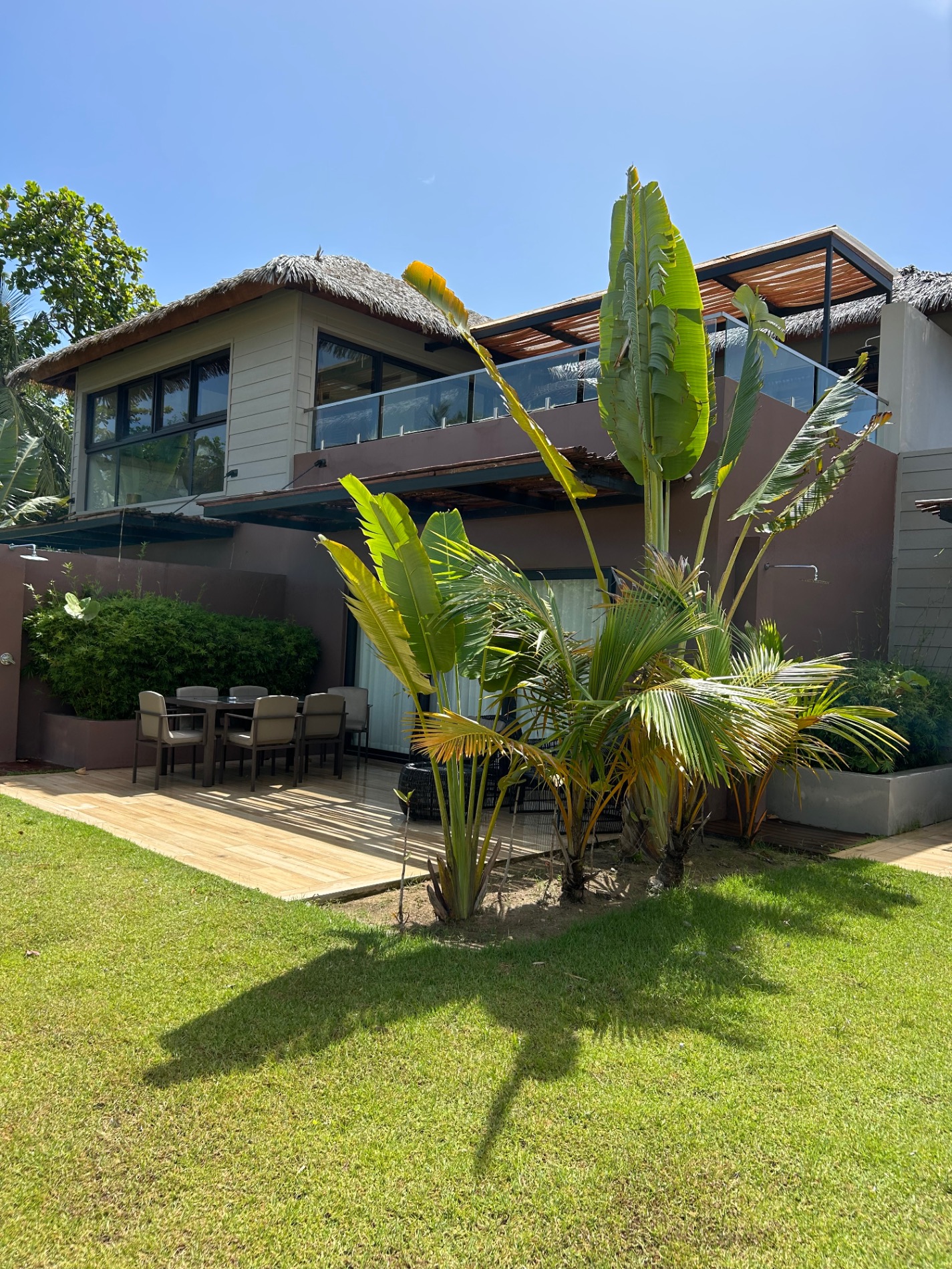 Modern two-story villa with thatched roof elements and tropical plants on manicured lawn