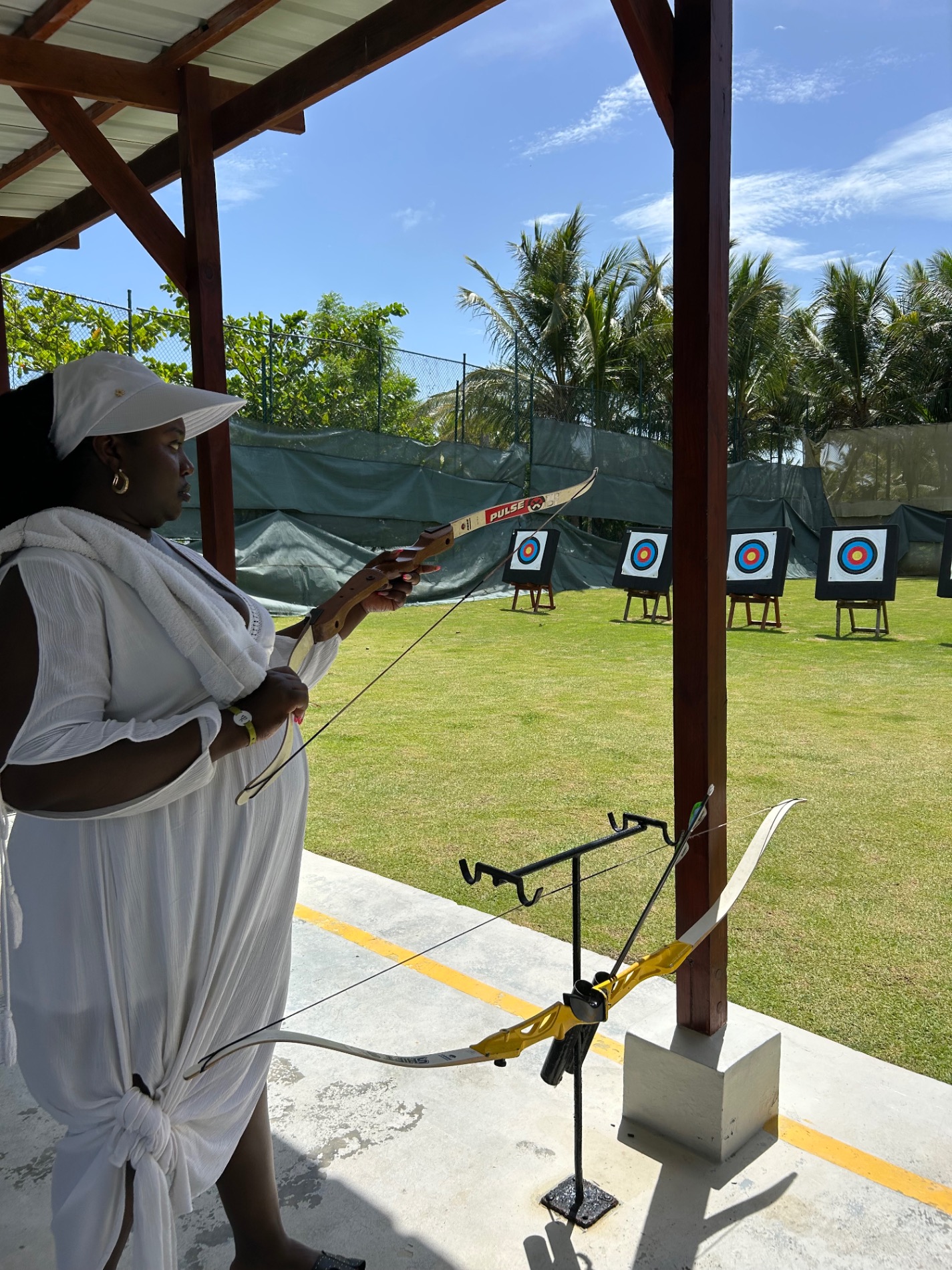 Woman holding bow and arrow at outdoor archery range with targets on grass field