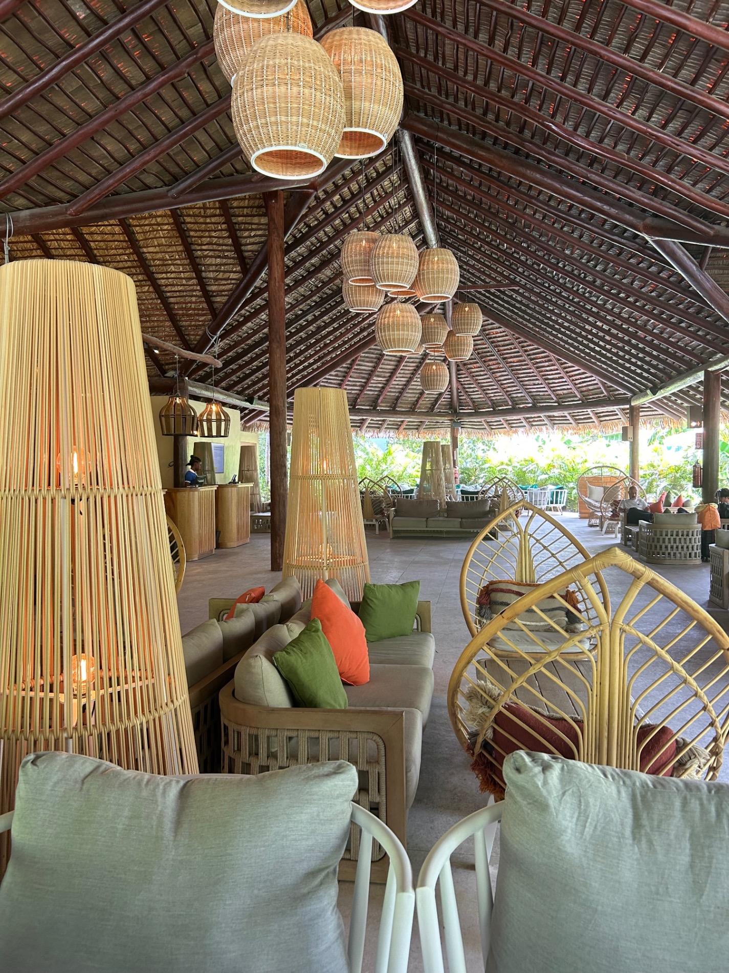 Woven basket pendant lights hanging from wooden beamed ceiling in covered resort lounge area