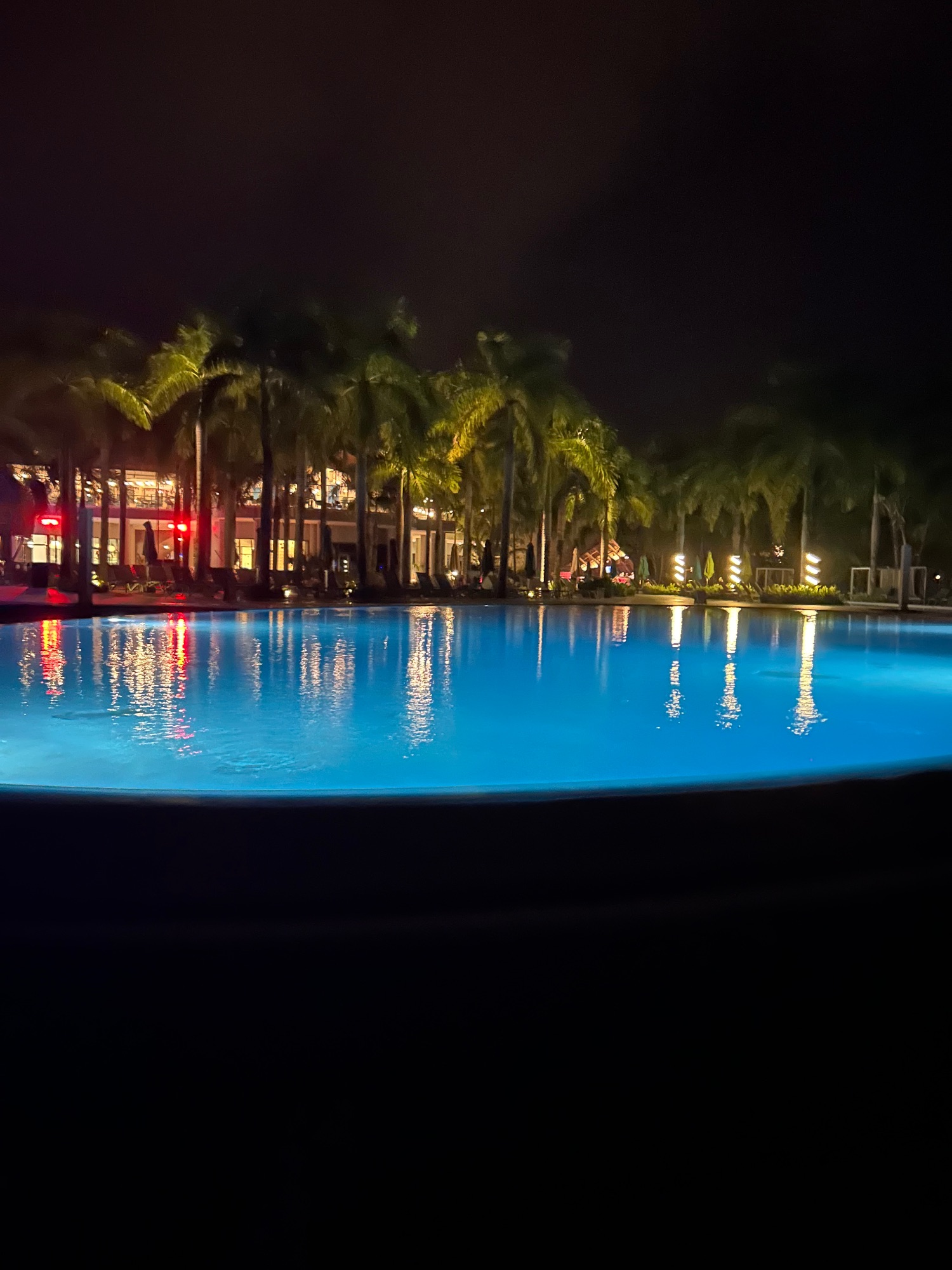 Resort pool glowing blue at night with palm trees and lit building in background
