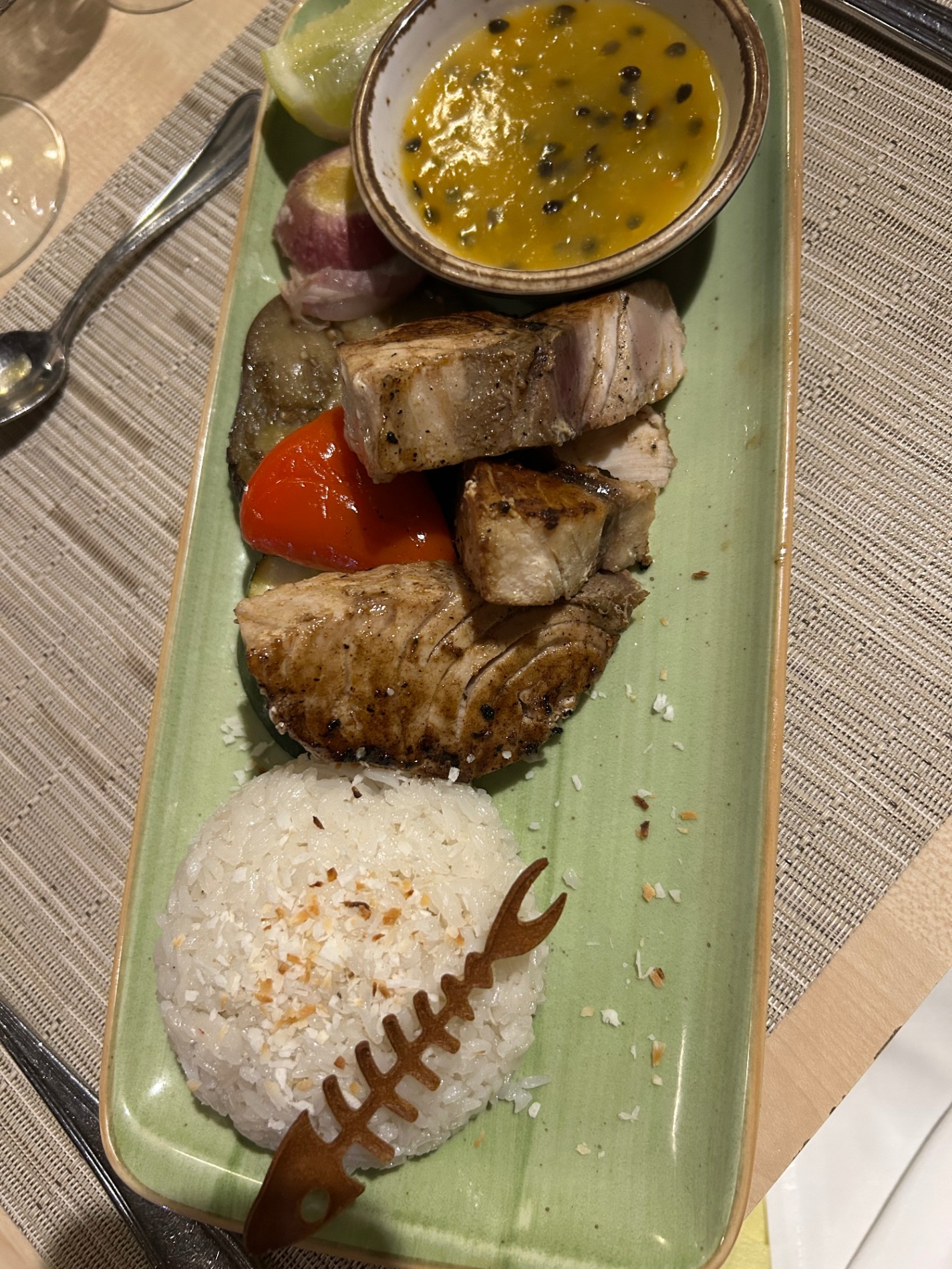 Plated meat dish with passion fruit sauce and rice on green rectangular plate