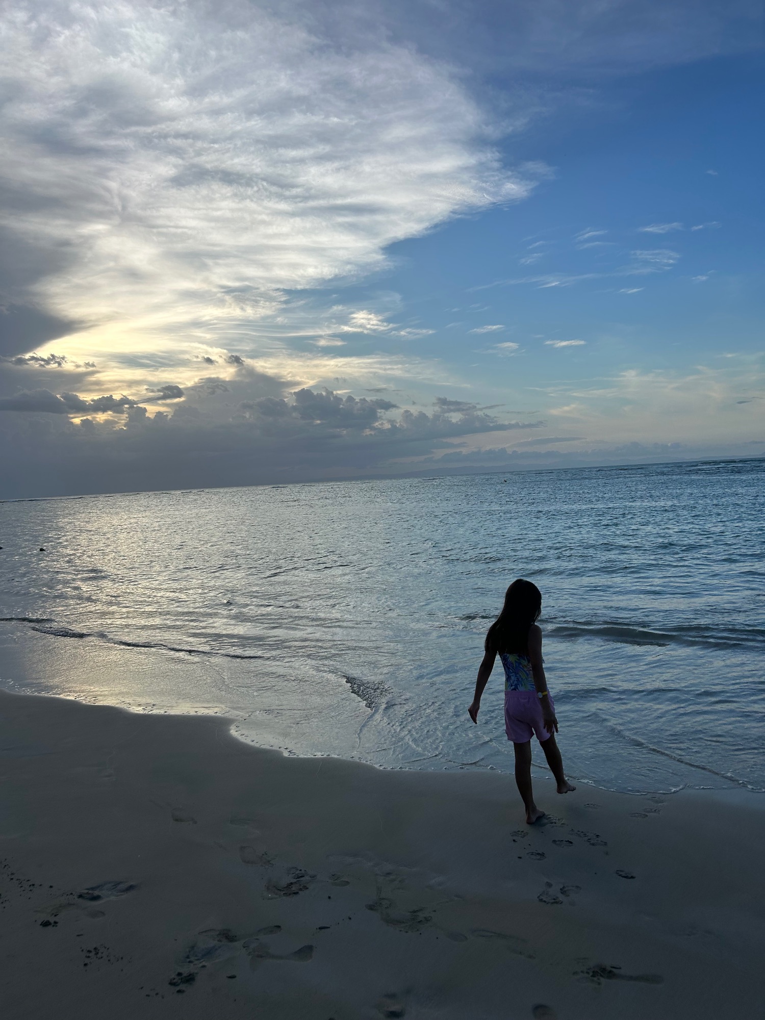 Sunset beach scene with child wading in calm ocean water and dramatic sky