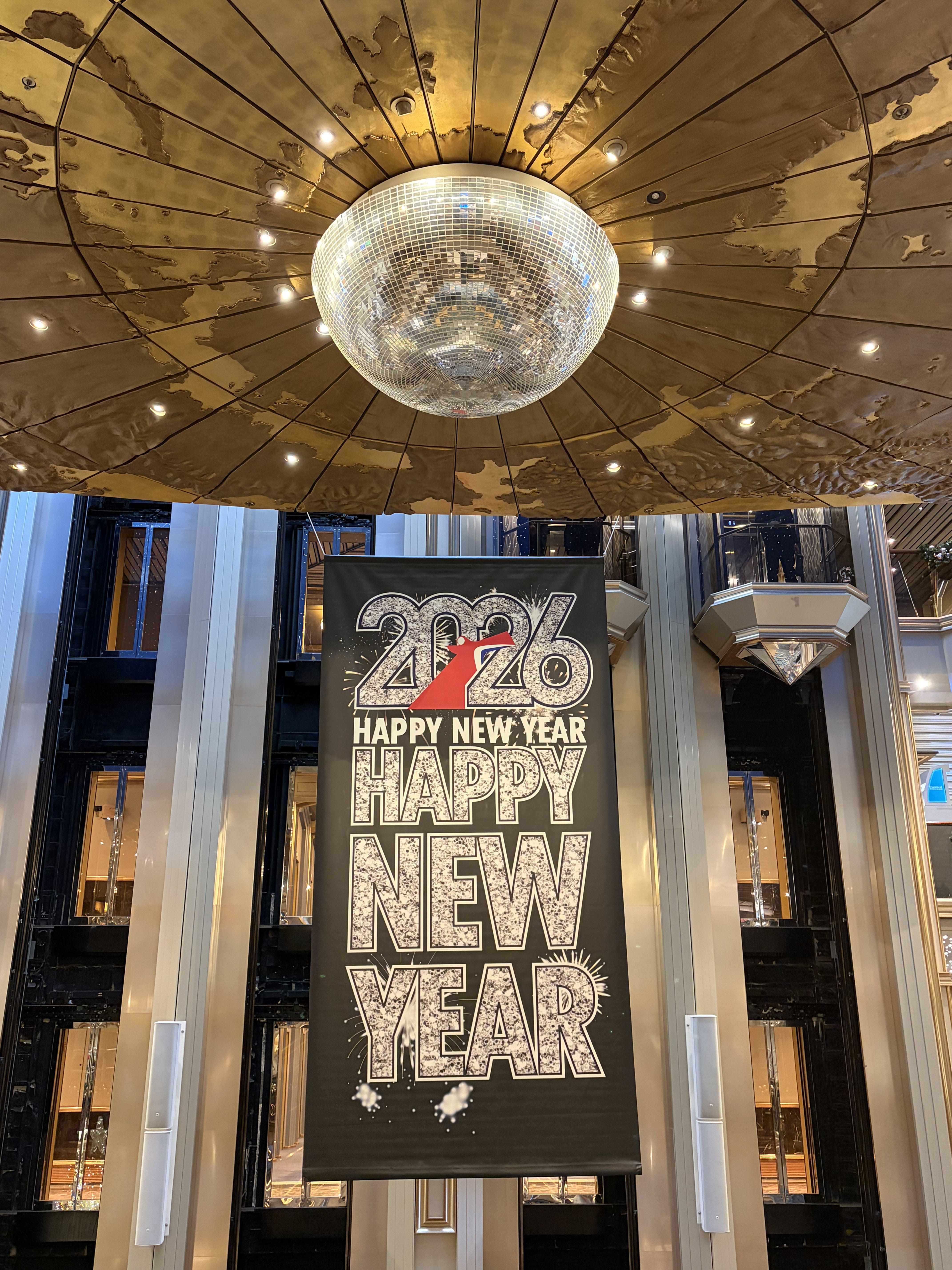 New Year 2026 celebration banner hanging in an elegant ship atrium with disco ball and railings