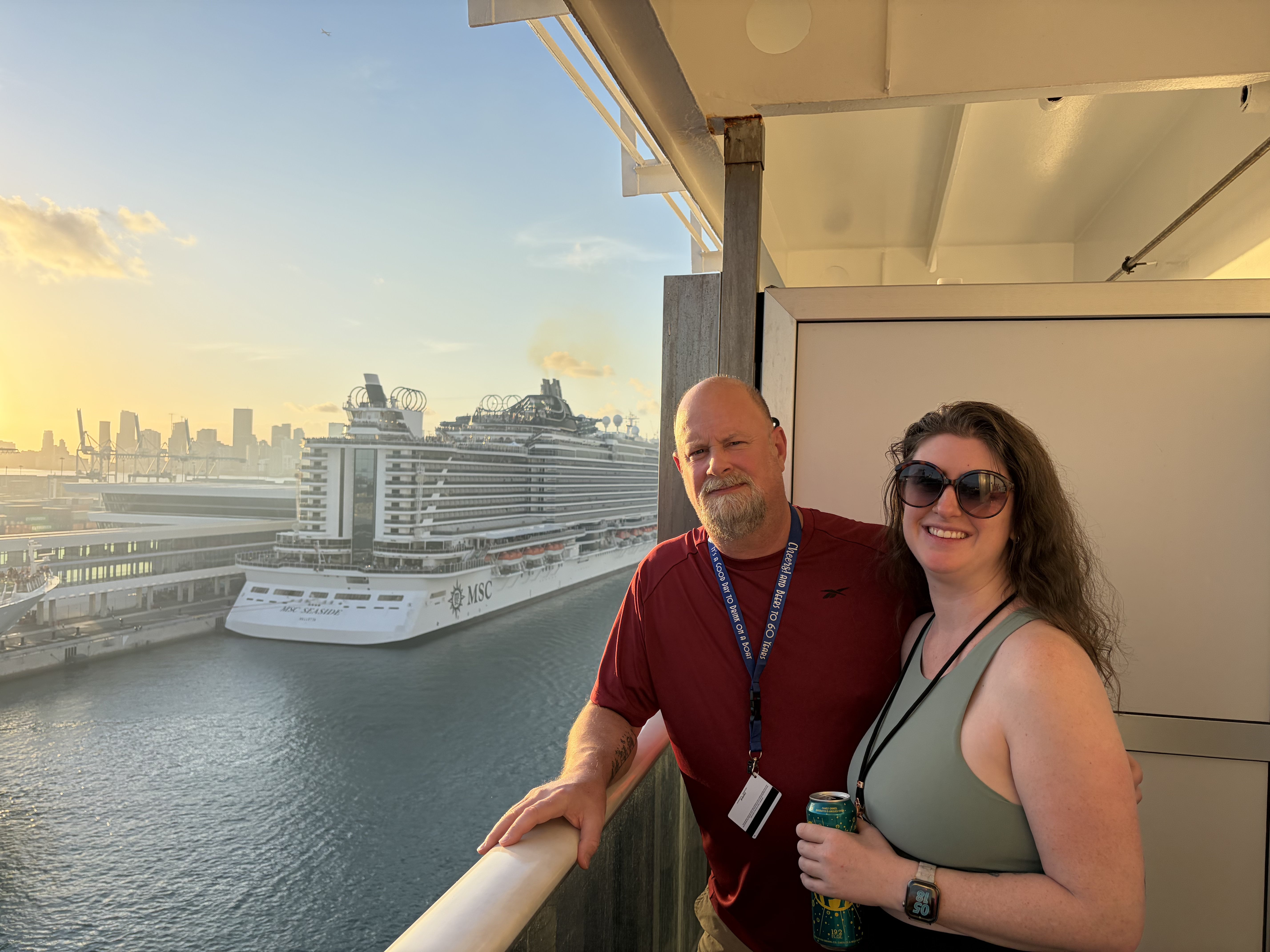 Man and woman posing on ship balcony with MSC cruise ship visible in port background