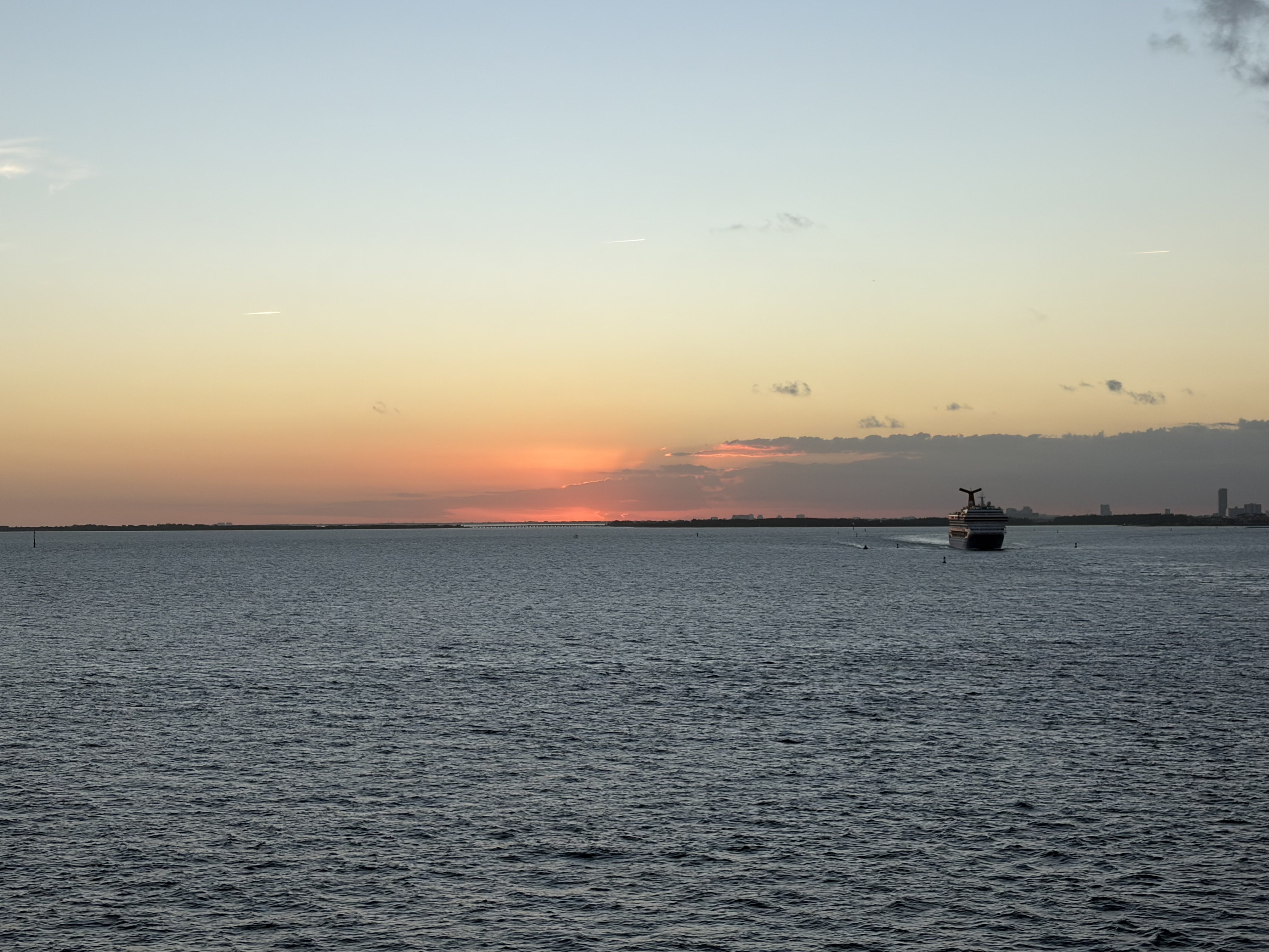 Sunset over calm ocean waters with small cruise ship silhouetted on horizon