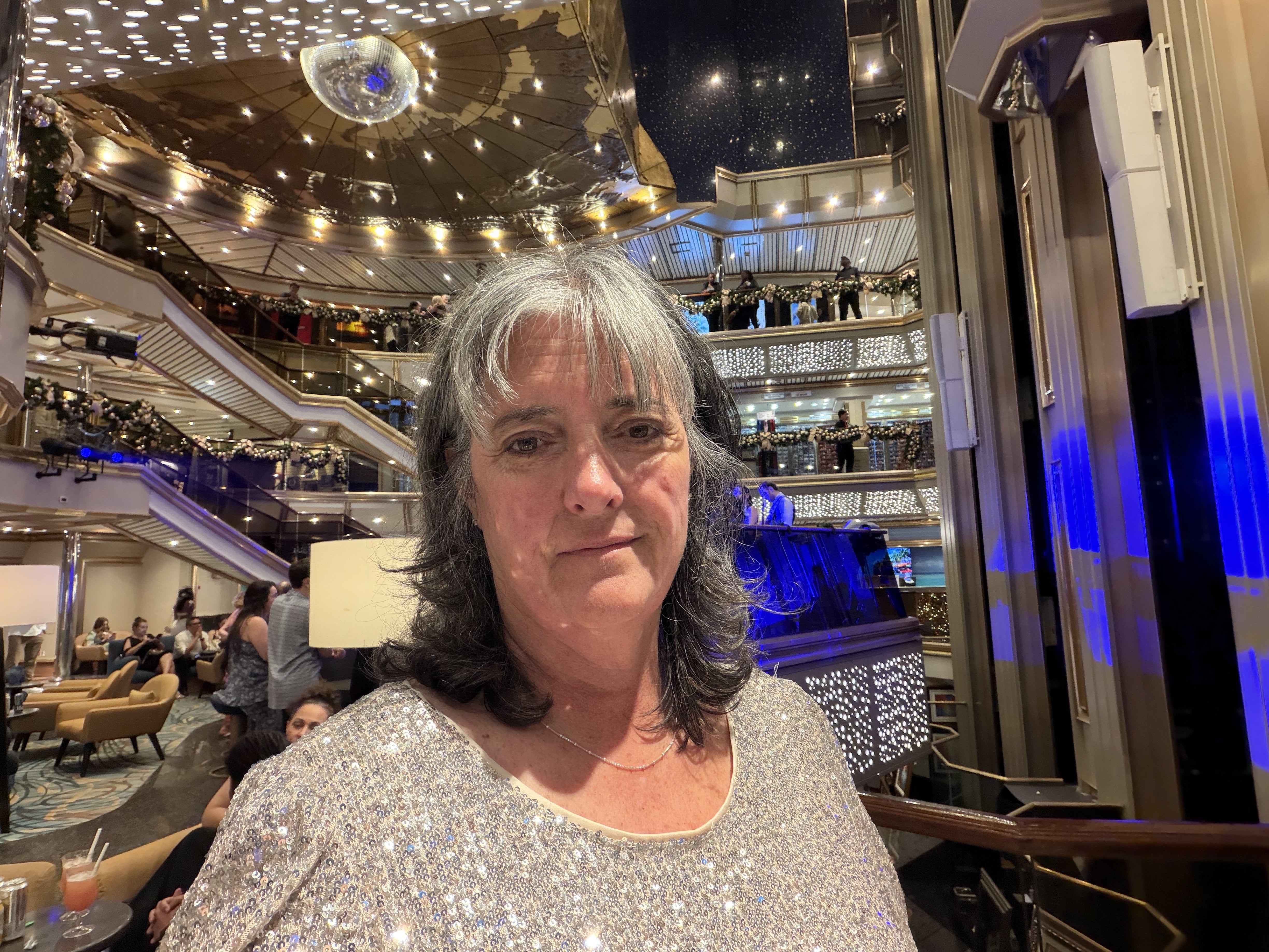 Woman in sequined top at ship's atrium with multi-level railings and holiday decorations