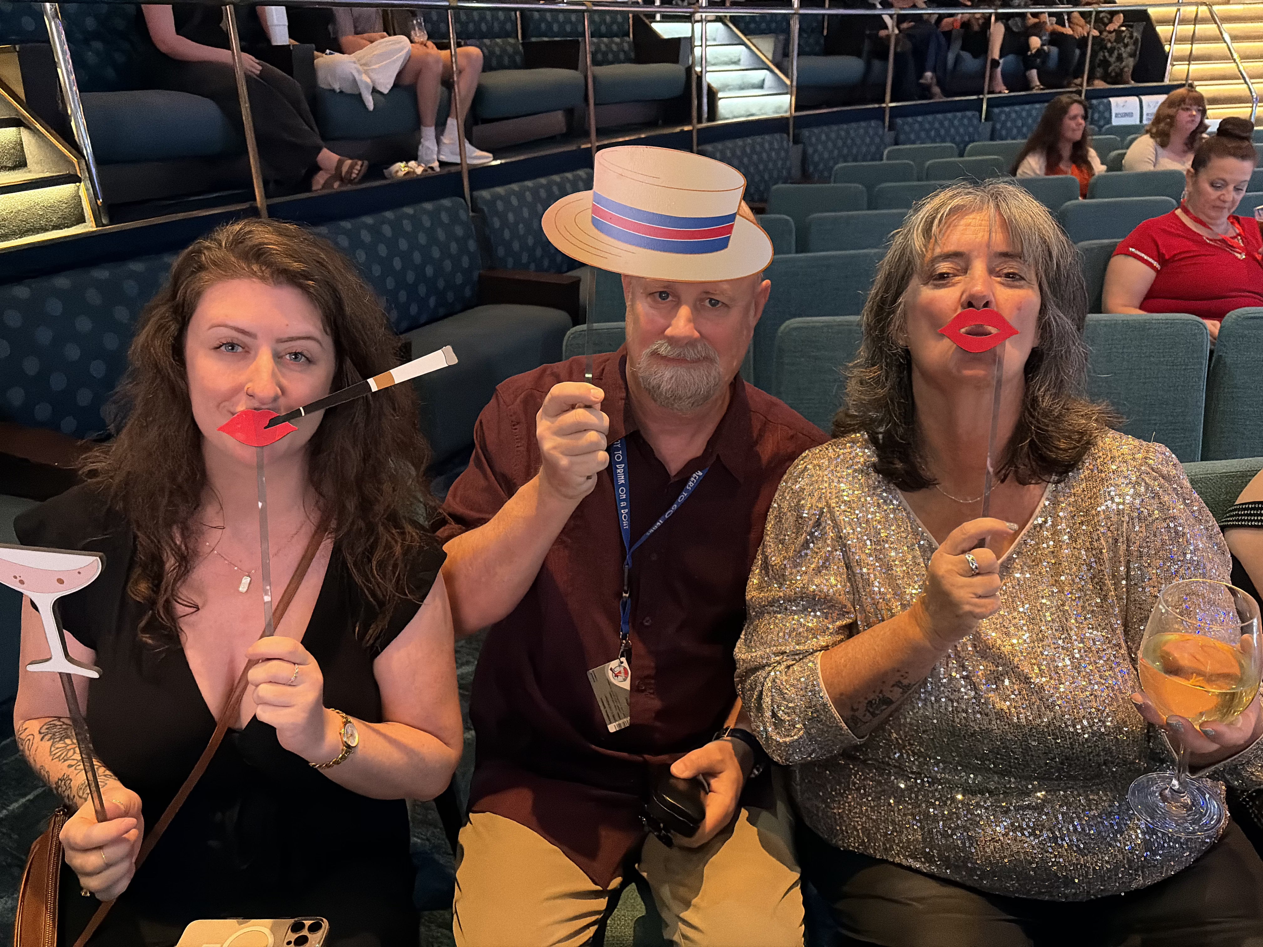 Three people holding novelty lips props in ship's theater during evening entertainment