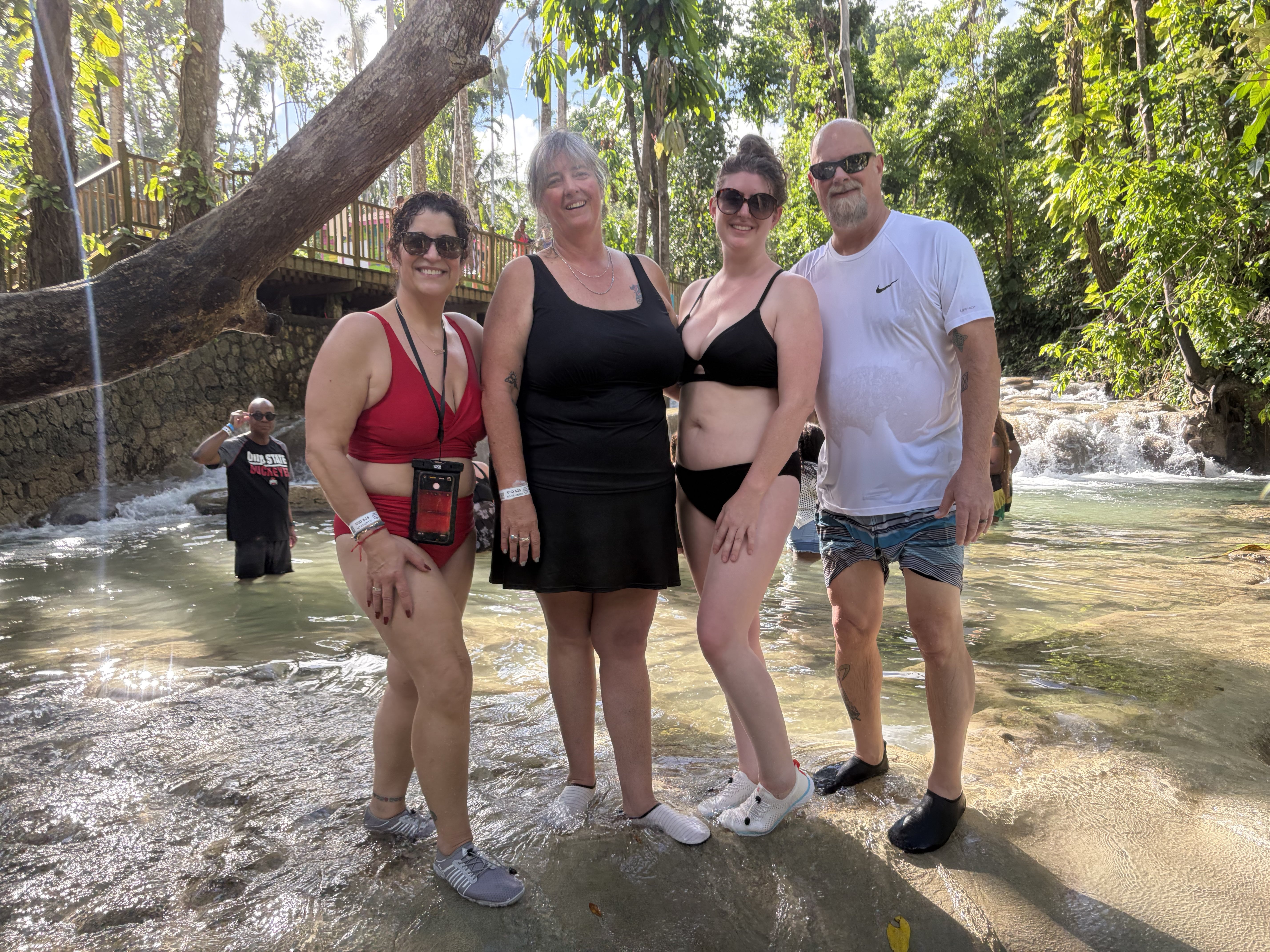 Four people standing in shallow turquoise water at Dunn's River Falls with cascades behind
