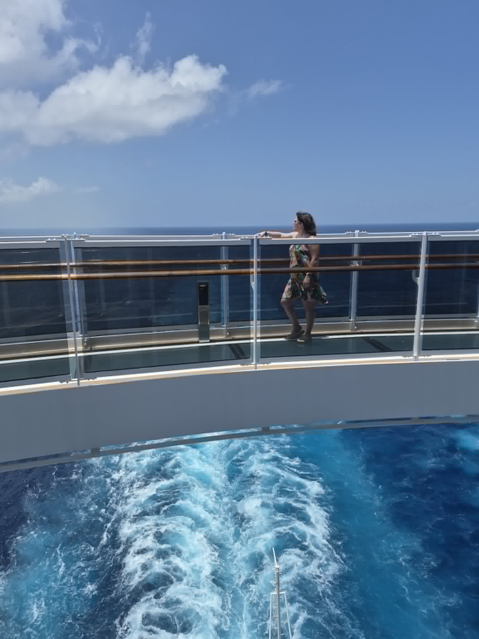 Woman in a colorful dress leans against a ship railing overlooking the ocean wake during a cruise