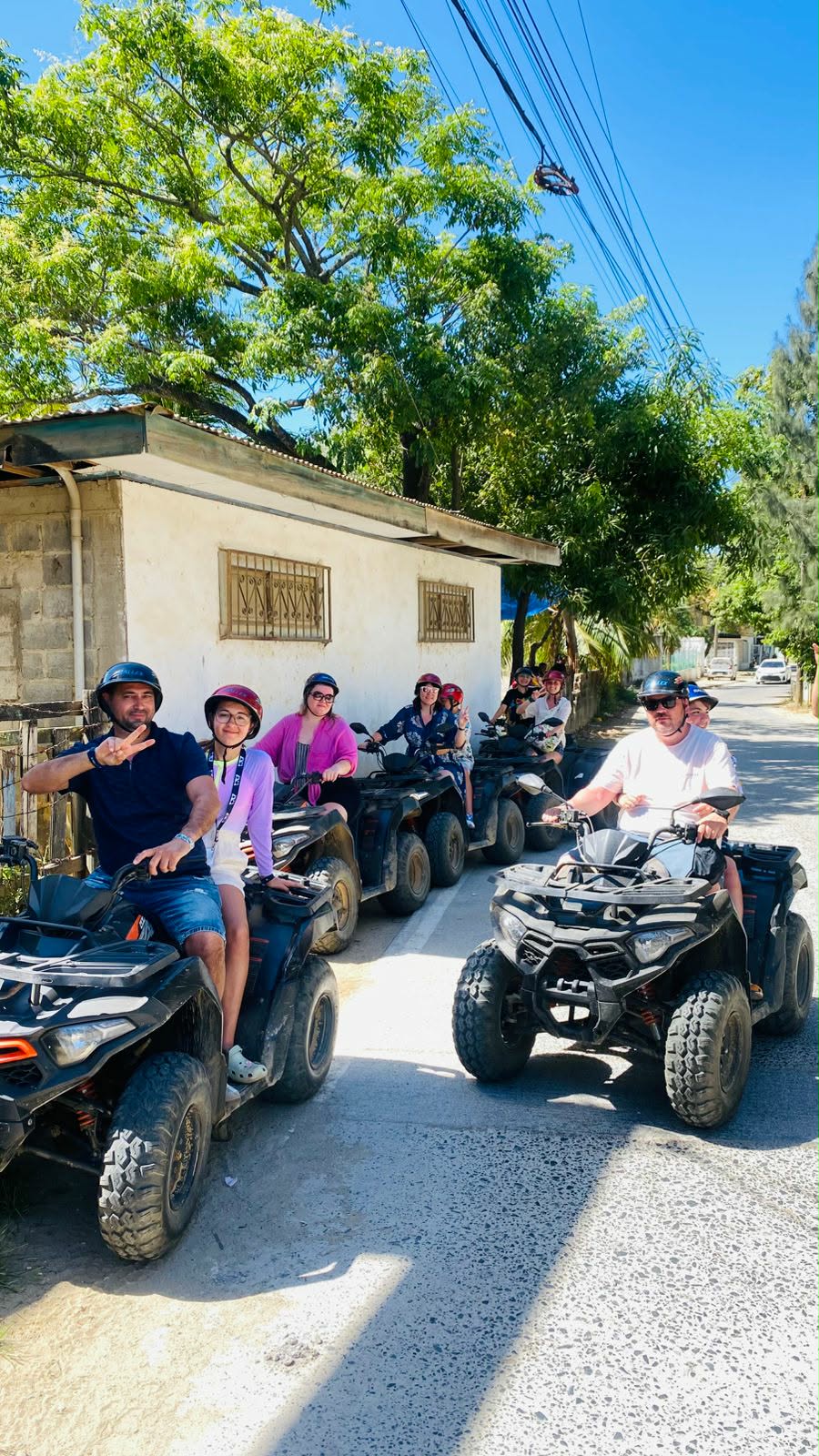 Cruise passengers in helmets ride ATVs down a tree-lined street during a Western Caribbean shore excursion