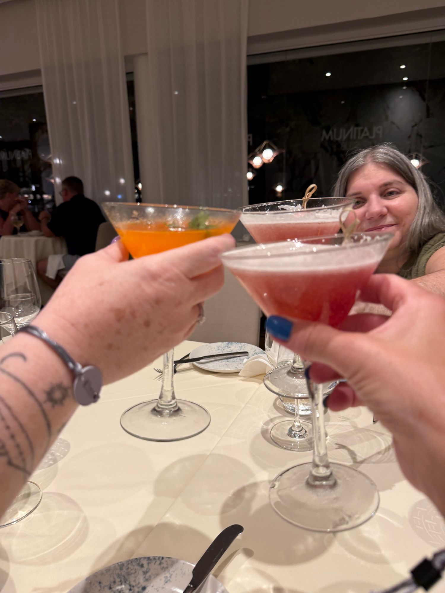 Two people clink colorful cocktails at an indoor dining event with elegant table settings