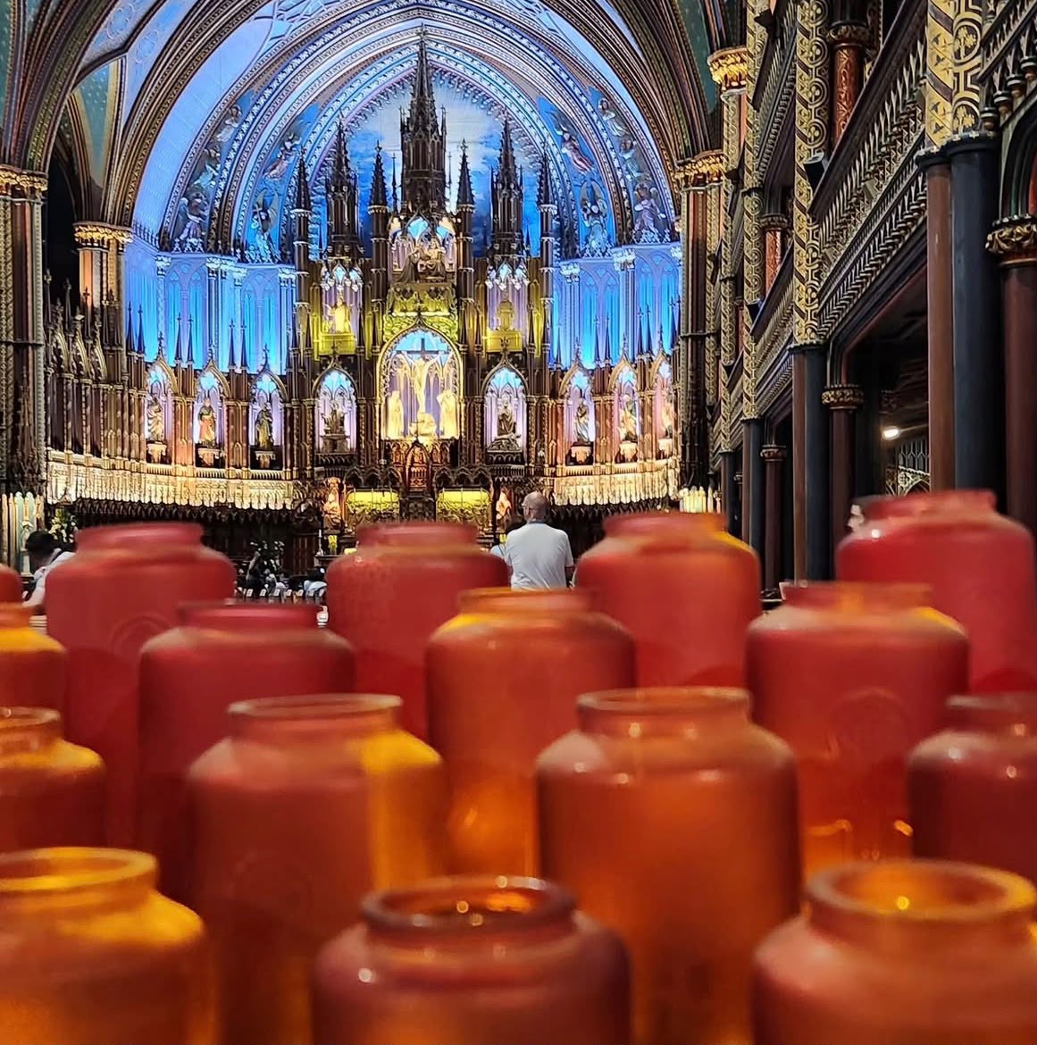 Interior of Notre-Dame-de-Québec Cathedral showing ornate Gothic architecture, blue vaulted ceiling, and red votive candles in foreground
